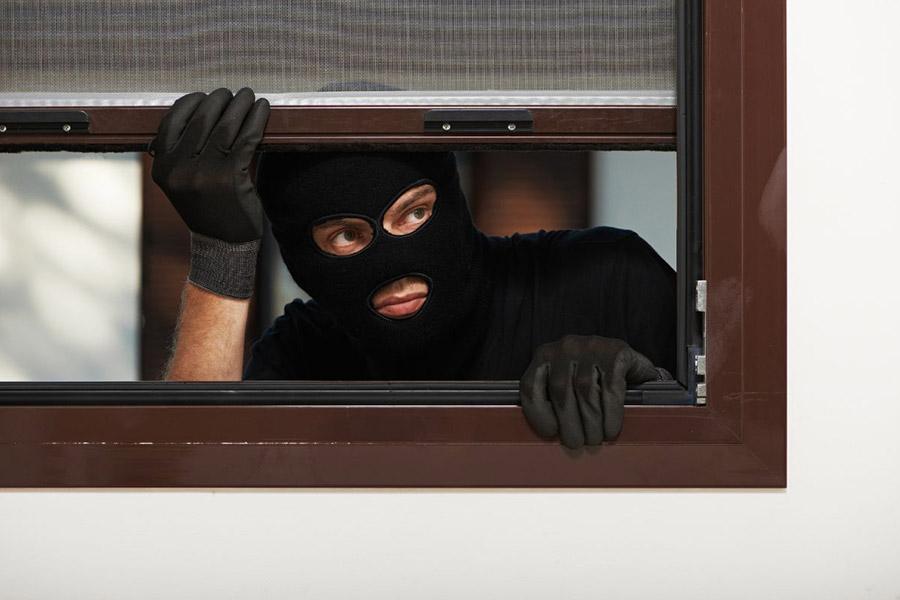 Zloděj v černé kukle nahlíží přes okno
